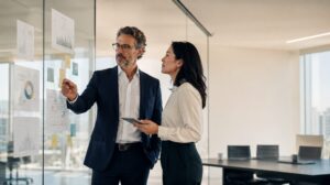 Two cross-functional colleagues collaborating on project planning using sticky notes on a glass wall